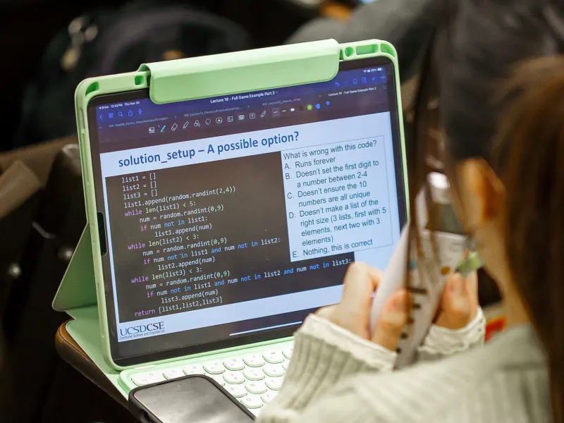 Student Considering GenAI Code. Student looking at their laptop. The laptop shows a question to them about GenAI produced code. Image Credit: Credit is David Baillot from UC San Diego Jacobs School of Engineering